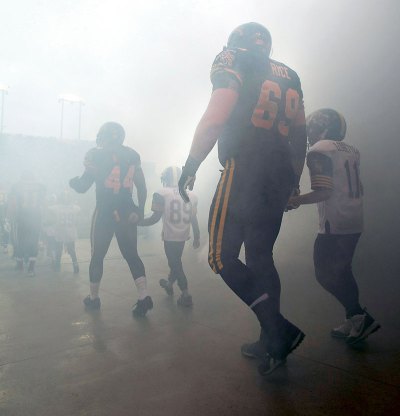 The Canadian Press
Brandonite Landon Rice of the Hamilton Tiger-Cats, escorted by a young football player, takes the field through smoke before the start of the CFL East Division final last week.