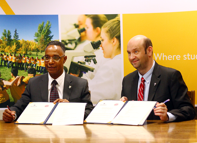 Tom Bateman/The Brandon Sun
Brandon University president Gervan Fearon, left, and Benjamin Robinson, assistant director of admission in Canada for St. George’s University in Grenada, sign a memorandum of understanding at BU on Tuesday. The agreement guaranteeing BU science grads entry into St. George’s is expected to send as many as six more students to the West Indies each year.