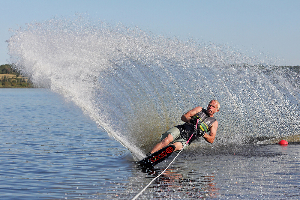 John Lepp carves across Lake Wahtopanah while slalom water skiing on a calm and clear Tuesday morning. Lepp learned how to waterski in his late 20s along with his brothers and taught his daughters Cassandra and Stefanie how to ski. Lepp and his daughters train every year in Florida.   (Tim Smith/The Brandon Sun)