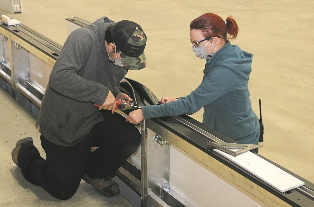 Perry Bergson/The Brandon Sun
Keystone Centre employees Kaylie McCorvie, right, and Jordan Armstrong fit the trim that goes into the slot where the glass sits in the new acrylic rink boards system being installed in Westoba Place on Tuesday.