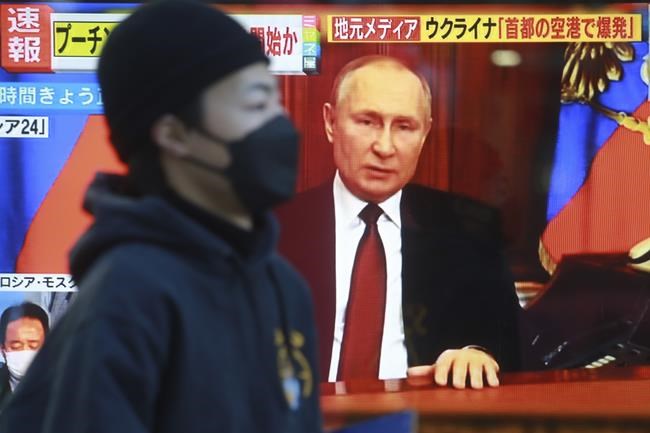 A man walks past a TV screen with image of Russia's President Vladimir Putin in Tokyo, Thursday, Feb. 24, 2022. As Russian troops attacked Ukraine, world leaders reacted Thursday with outrage, one called it