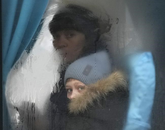 A woman and child peer out of the window of a bus as they leave Sievierodonetsk, the Luhansk region, eastern Ukraine, Thursday, Feb. 24, 2022. Russian President Vladimir Putin on Thursday announced a military operation in Ukraine and warned other countries that any attempt to interfere with the Russian action would lead to