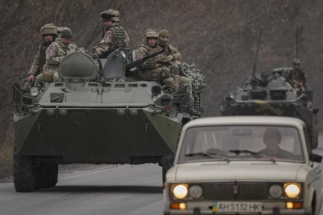 Ukrainian servicemen sit atop armored personnel carriers driving on a road in the Donetsk region, eastern Ukraine, Thursday, Feb. 24, 2022. Russian President Vladimir Putin on Thursday announced a military operation in Ukraine and warned other countries that any attempt to interfere with the Russian action would lead to