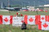 The Canadian Forces Snowbirds jets are seen in the background as a woman attaches a sign to a fence in Kamloops, B.C., Monday, May 18, 2020. The military's Snowbirds are being allowed back into the air after a deadly crash in May saw the aerobatic team's iconic jets grounded in British Columbia for more than three months. THE CANADIAN PRESS/Jonathan Hayward