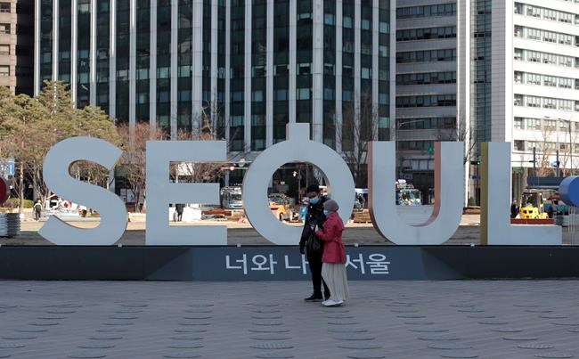 Visitors wearing face masks watch their smartphone near the display of South Korea's capital Seoul logo in downtown Seoul, South Korea, Sunday, Feb. 23, 2020. South Korea and China both reported a rise in new virus cases on Sunday, as the South Korean prime minister warned that the fast-spreading outbreak linked to a local church and a hospital in the country's southeast had entered a