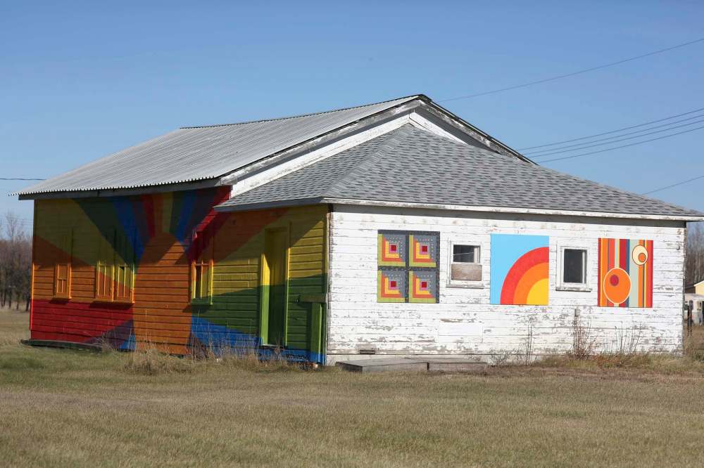 A building at the Harvest Sun Music Festival grounds is seen, with its left side painted by James Culleton and the wall to the right featuring barn quilts by three different artists.