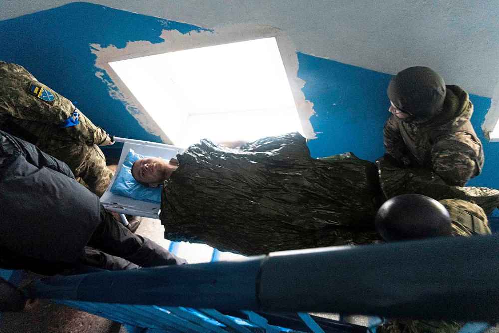 A Ukrainian serviceman and a civilian carry a wounded man who was injured by shelling in a hospital in Mariupol, Ukraine, Thursday, March 3, 2022. (Mstyslav Chernov / The Associated Press)
