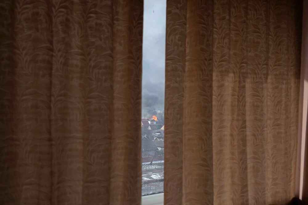 Seen through partially drawn curtains a house burns after shelling in Mariupol, Ukraine, Saturday, March 12, 2022. (Mstyslav Chernov / The Associated Press)