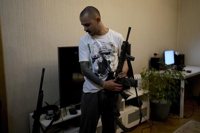 Viacheslav Drofa, known as Otoy, holds his rifle during an interview with The Associated Press at his home in Kyiv, Ukraine, Saturday, June 4, 2022. From the battlefronts of Ukraine comes rap music — filled with the anger and indignation of a young generation that, once the fighting is done, will certainly never forget and may never forgive.Ukrainian rapper-turned-volunteer soldier Otoy is putting the war into words and thumping baselines, tapping out lyrics under Russian shelling on his phone, with the light turned low to avoid becoming a target. It helps numb the nerve-shredding stress of combat. (AP Photo/Natacha Pisarenko)