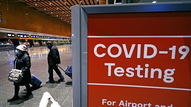 FILE - Travelers pass a sign near a COVID-19 testing site in Terminal E at Logan Airport, on Dec. 21, 2021, in Boston .The Biden administration is lifting its requirement that international air travelers to the U.S. take a COVID-19 test within a day before boarding their flights, easing one of the last remaining government mandates meant to contain the spread of the coronavirus.(AP Photo/Charles Krupa, File)