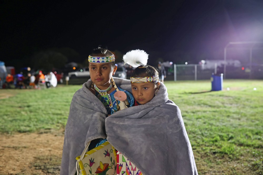 Cousins Gracie Meeches and Belle Mousseau share a blanket while watching dancers at the Sioux Valley Dakota Nation Pow Wow on Friday night. (Tim Smith/The Brandon Sun)