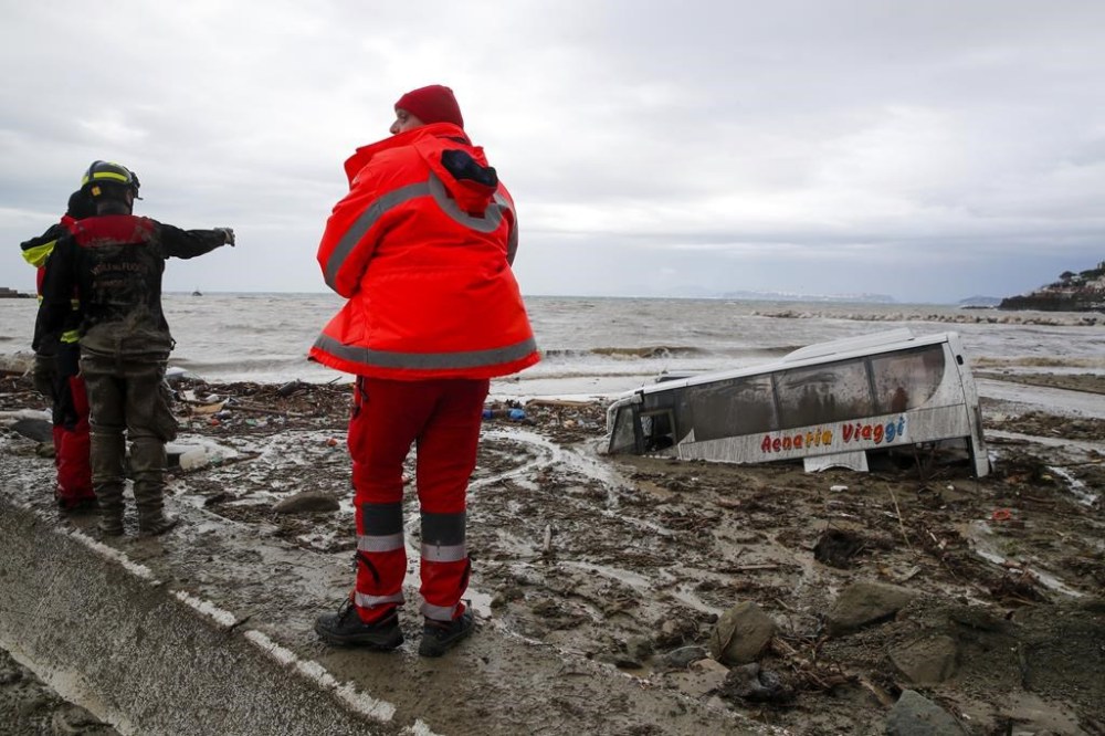 Rescuers look at a bus covered by mud after heavy rainfall triggered landslides that collapsed buildings and left as many as 12 people missing, in Casamicciola, on the southern Italian island of Ischia, Saturday, Nov. 26, 2022. Firefighters are working on rescue efforts as reinforcements are being sent from nearby Naples, but are encountering difficulties in reaching the island either by motorboat or helicopter due to the weather. (AP Photo/Salvatore Laporta)