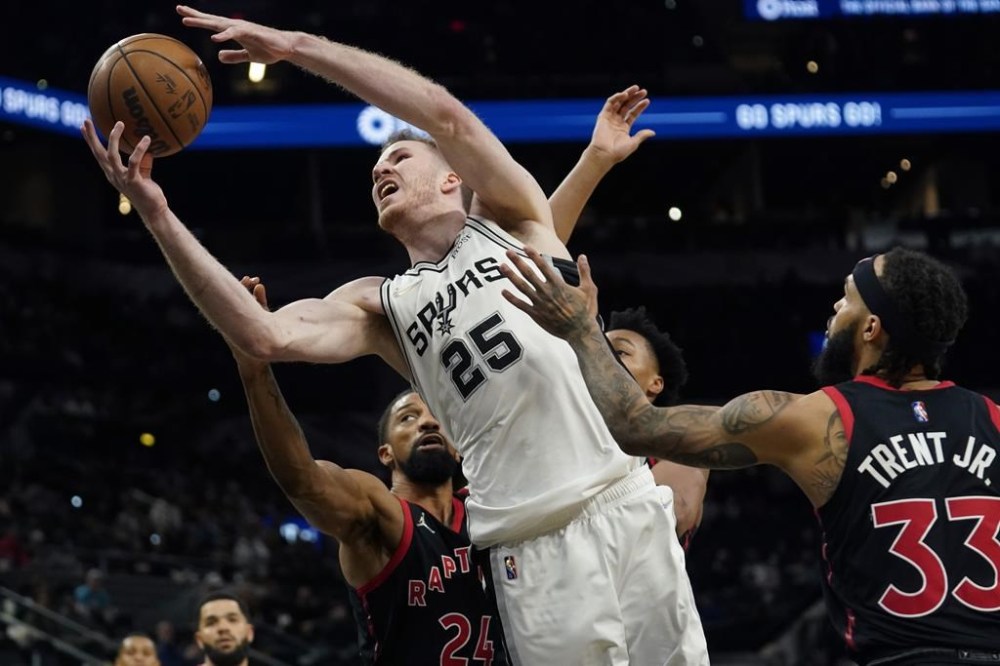 San Antonio Spurs center Jakob Poeltl (25) drives to the basket against Toronto Raptors center Khem Birch (24) and guard Gary Trent Jr. (33) during the second half of an NBA basketball game Wednesday, March 9, 2022, in San Antonio. (AP Photo/Eric Gay)