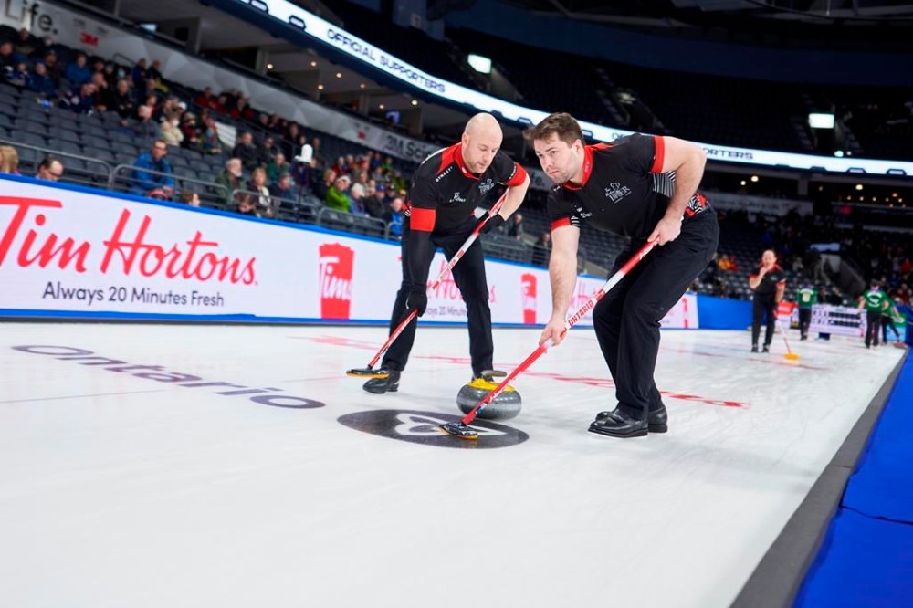 Ontario 3rd Ryan Fry (left) and lead Joey Hart sweep a rock during their match against P.E.I. at the 2023 Tim Hortons Brier at Budweiser Gardens in London, Ont. on Monday, March 6, 2023.THE CANADIAN PRESS/ Geoff Robins