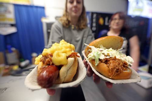 Lexi Brown, an employee at one of the two Smoked and Sauced Mobile BBQ booths at the Royal Manitoba Winter Fair, holds out a pair of sandwich favourites: a Pac-Mac Dog (left) and pulled pork with coleslaw (right). (Matt Goerzen/The Brandon Sun)