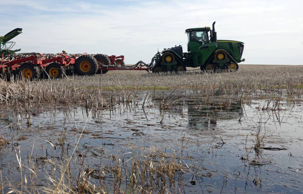 A tractor and seeding equipment are reflected in a pool of standing water in a field north of Rivers. A new tool from the Manitoba Forage and Grassland Association allows producers to monitor flood and drought conditions. (File)