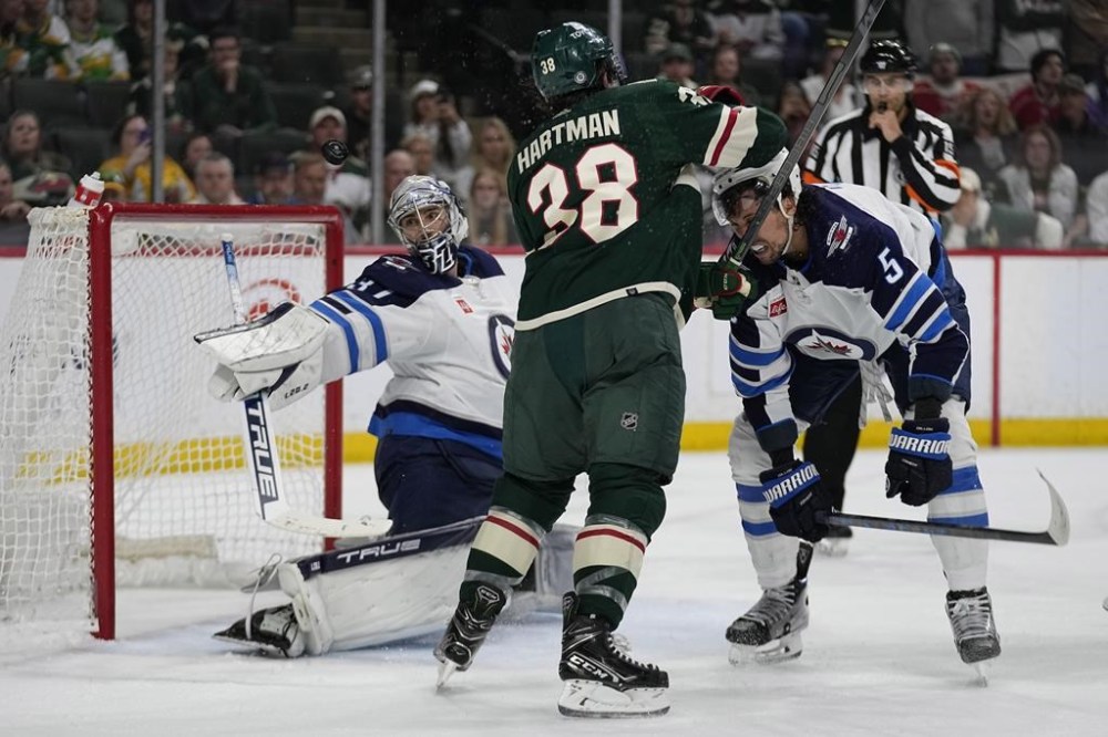 Winnipeg Jets goaltender Connor Hellebuyck, left, defends the goal as a fight begins between Minnesota Wild right wing Ryan Hartman (38) and Winnipeg Jets defenseman Brenden Dillon, right, during the third period of an NHL hockey game, Tuesday, April 11, 2023, in St. Paul, Minn. (AP Photo/Abbie Parr)