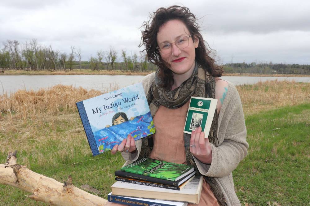 \Winnipeg educator Ash Alberg sits next to the Assiniboine River in Brandon on Thursday with some of their favourite books on the art and science of natural dyes. Alberg is in the middle of developing a brand new curriculum on natural dyes with the aim of making it widely available in Manitoba by the 2024-25 school year. (Kyle Darbyson/The Brandon Sun)