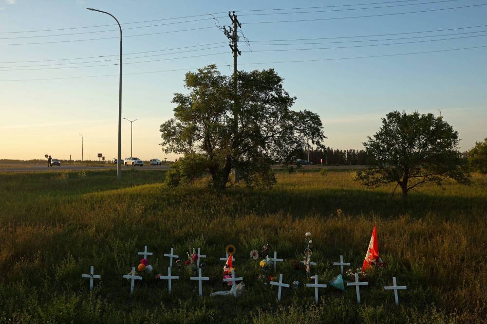 A memorial to the June 15 collision between a bus and a semi-truck that claimed the lives of 17 passengers sits just south of the intersection of the Trans-Canada Highway and Highway 5 as RCMP officers and tow truck operators work at the scene of a three-vehicle collision at the same intersection on Monday evening. (Tim Smith/The Brandon Sun)