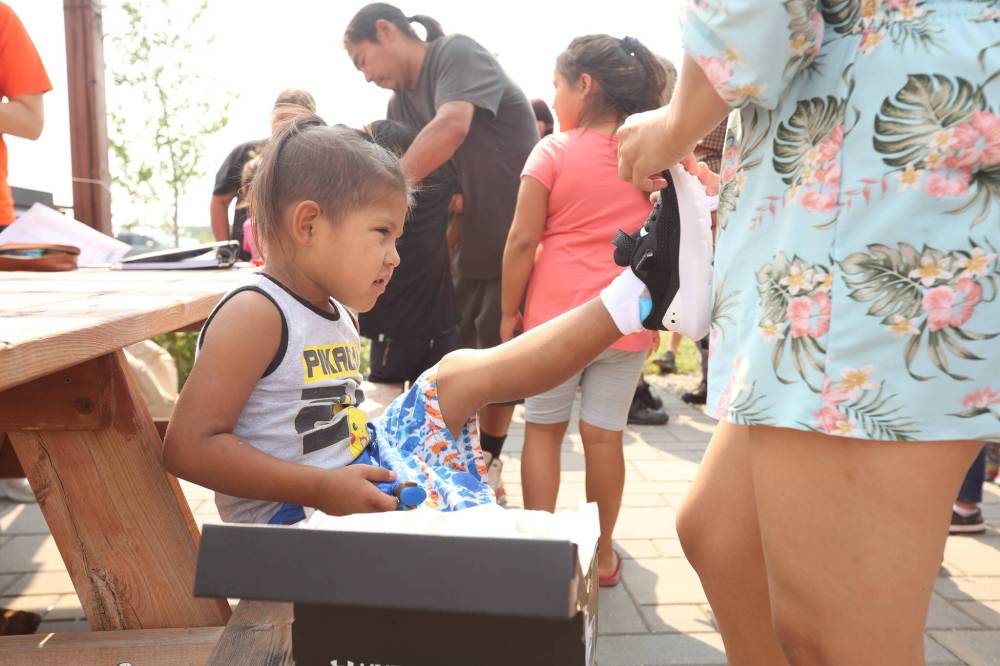 Kenai Keesick gets help trying on a pair of Under Armour shoes at the Birdtail Sioux First Nation Healing Garden.