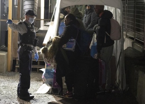 An RCMP officer instructs asylum seekers as they wait for processing after crossing the border at Roxham Road from New York into Canada, Friday March 24, 2023, in Champlain, N.Y. The closure of a rural southern Quebec road used by thousands of asylum seekers to enter Canada from the United States hasn't stopped would-be refugees from arriving, federal data shows. THE CANADIAN PRESS/Ryan Remiorz