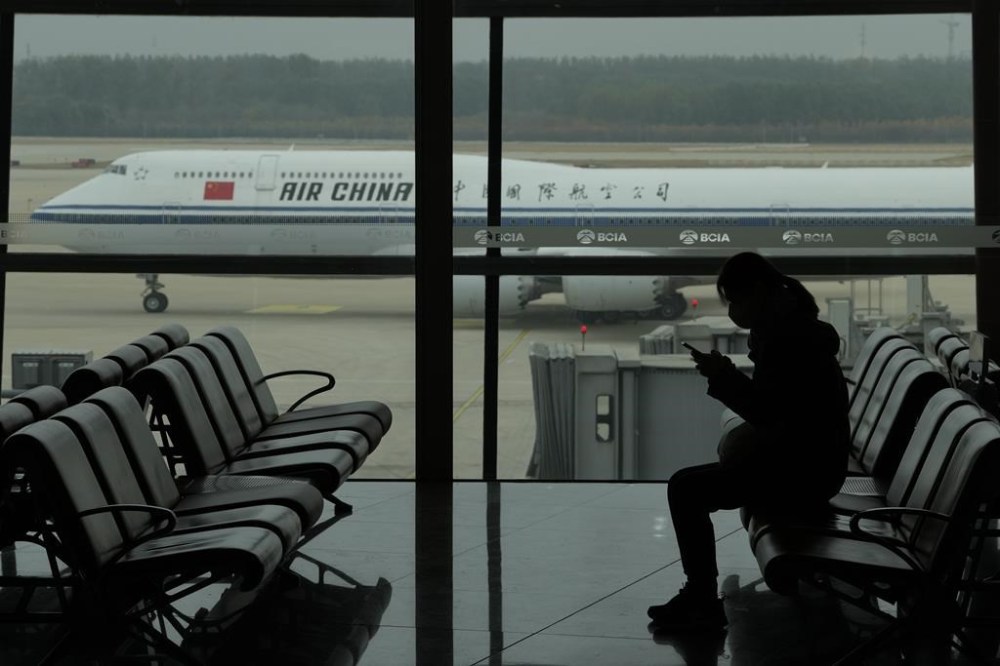 Beijing and Ottawa are in talks over how to increase flights between Canada and China, following an American deal in June. A passenger checks her phone as an Air China passenger jet taxis past at the Beijing Capital International airport in Beijing, Saturday, Oct. 29, 2022. THE CANADIAN PRESS/AP-Ng Han Guan