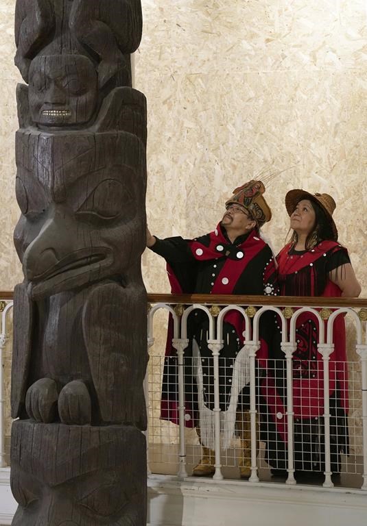 Earl Stephens, who has the Nisga'a cultural name Chief Ni'is Joohl, left, and Pamela Brown from the Nisga'a nation pose beside the 11-metre tall memorial pole, during a visit to the National Museum of Scotland, ahead of its return to what is now British Columbia, in Edinburgh, Monday, Aug. 28, 2023. Members of a Canadian First Nation held a spiritual ceremony on Monday at a Scottish museum to begin the homeward journey of a totem pole stolen almost a century ago. (Andrew Milligan/PA via AP)