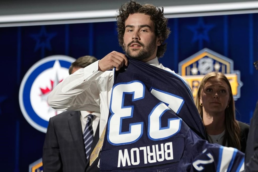 Colby Barlow puts on a Winnipeg Jets jersey, Wednesday, June 28, 2023, in Nashville, Tenn. The Jets have signed first-round pick Barlow on a three-year, entry-level contract. THE CANADIAN PRESS/AP-George Walker IV