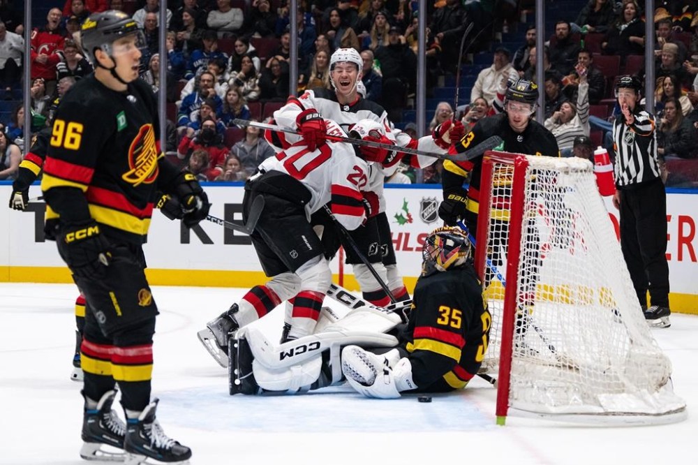 New Jersey Devils' Nathan Bastian (14) and Michael McLeod (20) celebrate McLeod's goal on Vancouver Canucks goaltender Thatcher Demko (35) as Vancouver's Quinn Hughes (43) watches during the first period of an NHL hockey game in Vancouver on Tuesday, Dec. 5, 2023. THE CANADIAN PRESS/Ethan Cairns
