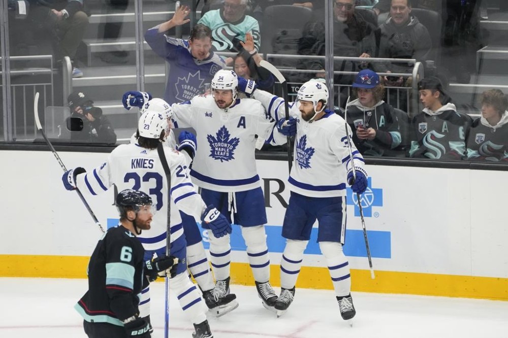 Toronto Maple Leafs centre Auston Matthews (34) celebrates with teammates, including left wing Matthew Knies (23), right wing Mitchell Marner (16) and defenceman Timothy Liljegren (37), after scoring as Seattle Kraken defenceman Adam Larsson (6) skates away during the first period of an NHL hockey game Sunday, Jan. 21, 2024, in Seattle. (AP Photo/Lindsey Wasson)