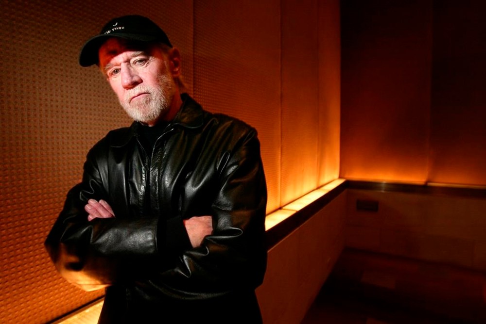 FILE - Actor and comedian George Carlin poses in a New York hotel March 19, 2004. Carlin's estate has filed a lawsuit against the media company behind a fake hourlong comedy special that purportedly uses artificial intelligence to recreate the late standup comic’s style and material. The lawsuit filed in federal court in Los Angeles on Thursday, Jan. 25, 2024, asks that a judge order the podcast outlet, Dudesy, to immediately take down the audio special, “George Carlin: I'm Glad I'm Dead,