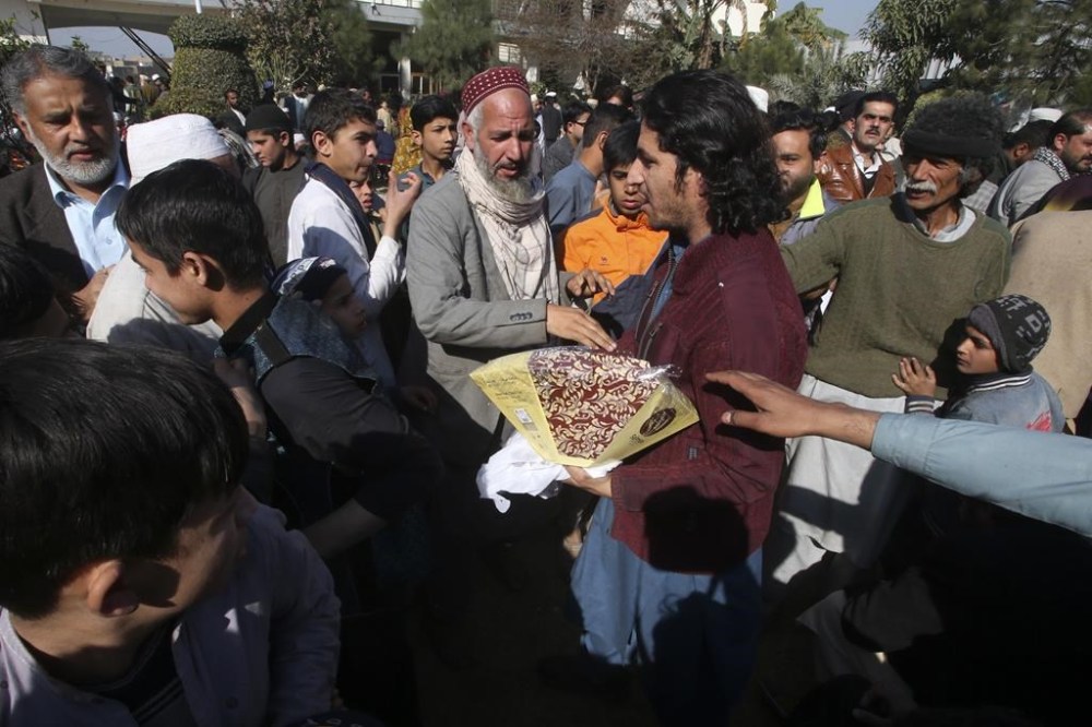 A supporter of an independent candidate distributes traditional sweet to others as they celebrate the victory of his leader in the parliamentary elections, in Peshawar, Pakistan, Friday, Feb. 9, 2024. The results of Pakistan's elections were delayed a day after the vote that was marred by sporadic violence, a mobile phone service shutdown and the sidelining of former Prime Minister Imran Khan and his party. (AP Photo/Muhammad Sajjad)