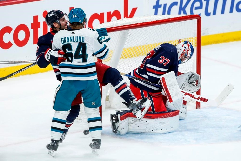 The puck trickles wide as Winnipeg Jets goaltender Connor Hellebuyck (37) saves the shot and Dylan DeMelo (2) defends against San Jose Sharks' Mikael Granlund (64) during second period NHL action in Winnipeg on Wednesday, February 14, 2024. THE CANADIAN PRESS/John Woods