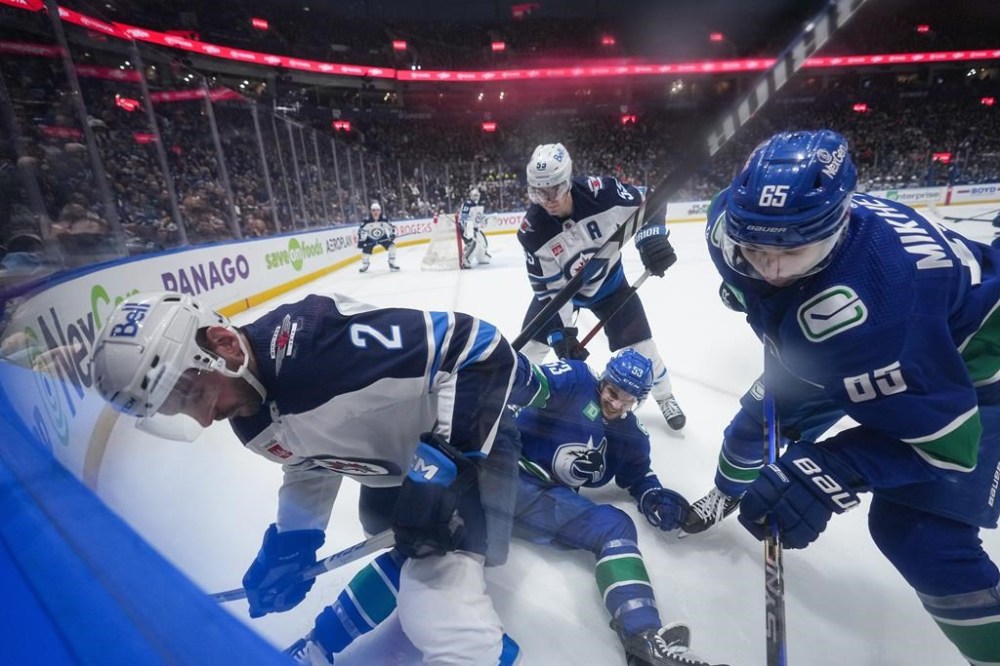 Winnipeg Jets' Dylan DeMelo (2) vies for the puck against Vancouver Canucks' Ilya Mikheyev (65) and Teddy Blueger (53) as Winnipeg's Mark Scheifele, back centre, watches during the first period of an NHL hockey game in Vancouver, on Saturday, Feb. 17, 2024. THE CANADIAN PRESS/Darryl Dyck