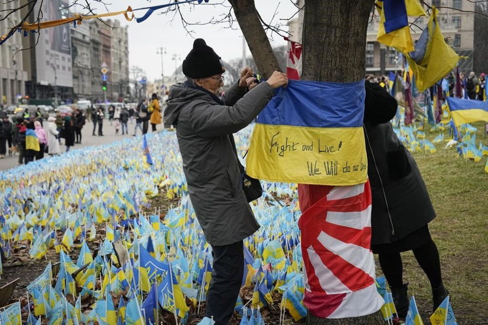 Fuminori Tsuchiko, a 75-year-old Japanese volunteer, ties a Ukrainian flag to a tree at the memorial site for those killed during the war, near Maidan Square in central Kyiv, Ukraine, Saturday, Feb. 24, 2024. Ukraine is marking two years since Russia's full-scale invasion with a somber mood hanging over the country. On the battlefield, Ukrainian troops are running low on ammunition as they hope for further Western aid. (AP Photo/Efrem Lukatsky)