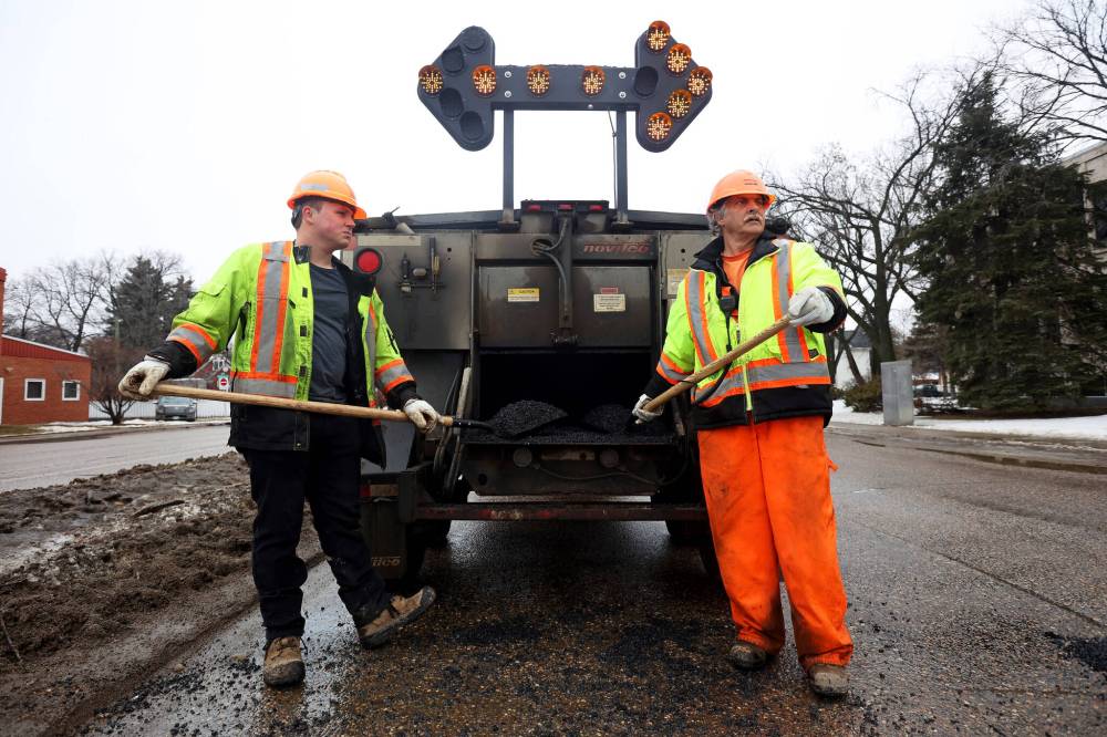 Nathaniel Hegg and Harry Davis with Manitoba Transportation and Infrastructure watch for a break in traffic to fill potholes at the intersection of 18th Street and Victoria Avenue in Brandon on Monday. (Tim Smith/The Brandon Sun)