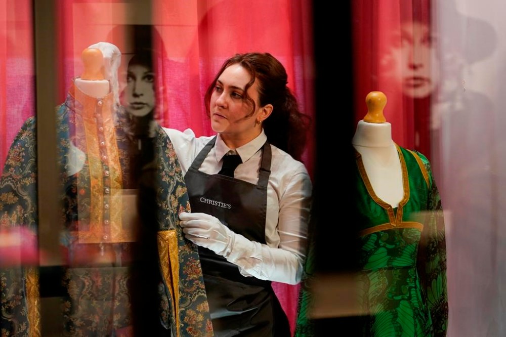 A member of staff poses next to dresses from The Pattie Boyd Collection, at Christie's, in London, Thursday, March 14, 2024. The dresses is estimated to sell within a range of £800-1,500. (AP Photo/Alberto Pezzali)