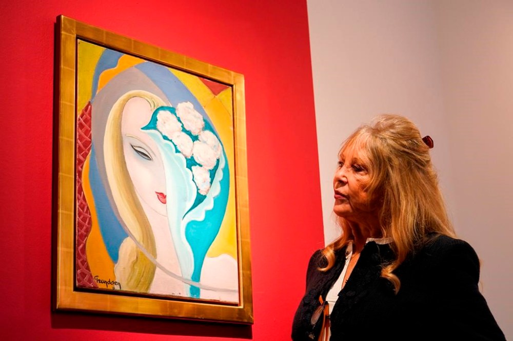Pattie Boyd poses next to the original artwork by E. Frandsen De Schomberg, used for the cover of Derek and the Dominoes album 'Layla and Other Assorted Love Songs' as part of The Pattie Boyd Collection at Christie's, in London, Thursday, March 14, 2024. The artwork is estimated to sell £40,000-60,000. (AP Photo/Alberto Pezzali)