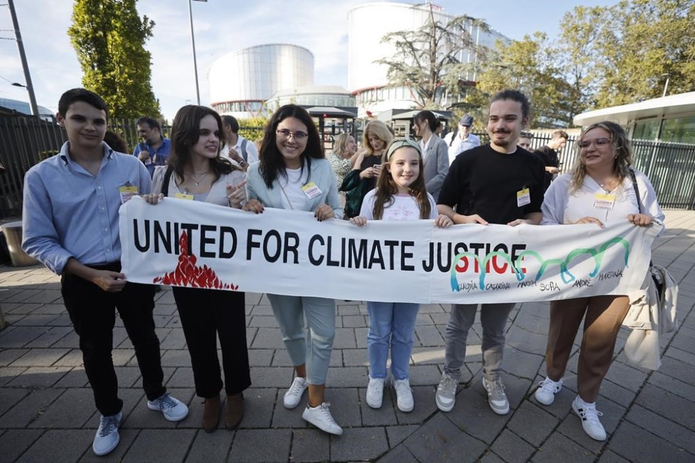 FILE - Mariana, center right, Claudia Agostinho, right, Martim Agostinho, second right, Sofia Oliveira, second left, her brother Andre, left, with Catarine Mota, pose with a banner outside the European Court of Human Rights on Sept. 27, 2023 in Strasbourg, eastern France. Europe’s highest human rights court will rule Tuesday April 9, 2024 on a group of landmark climate change cases aimed at forcing countries to meet international obligations to reduce greenhouse gas emissions. (AP Photo/Jean-Francois Badias, File)