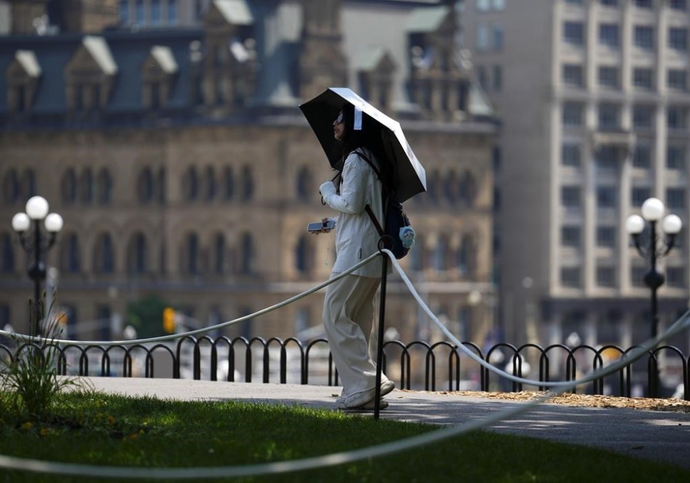 Dressing for the summer to stay and look cool is a little more than picking out a white T-shirt and a pair of shorts. It involves choosing the right fabric, making sure the fit is perfect and remembering to hydrate. A tourist carries an umbrella as they visit Parliament Hill in Ottawa on Tuesday, June 18, 2024, as temperatures hit 32C in what meteorologists are calling a heat dome. THE CANADIAN PRESS/Sean Kilpatrick