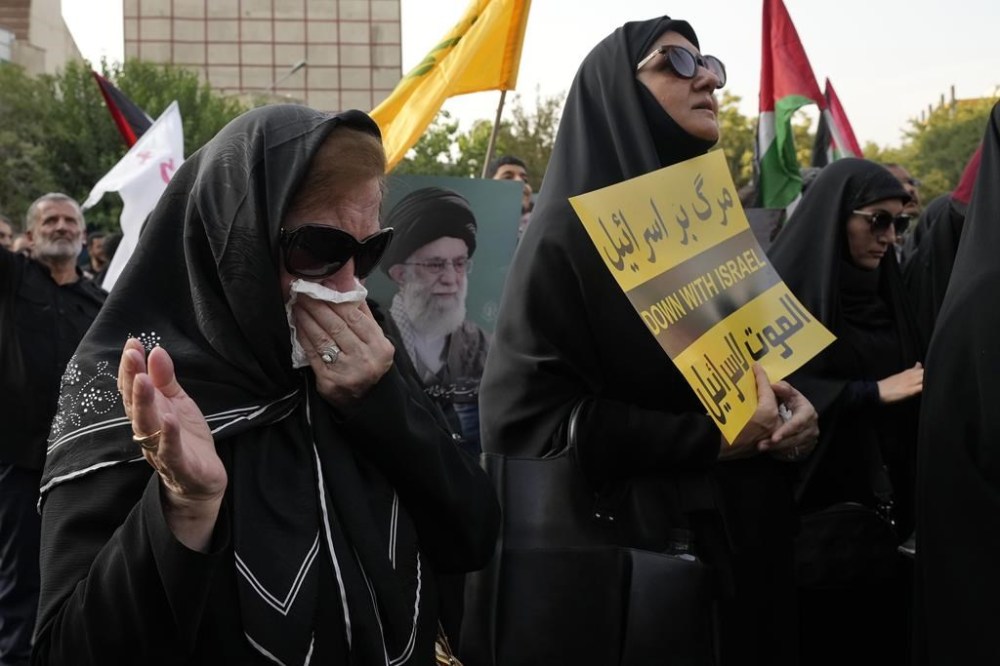 A protester weeps as the others hold an anti-Israeli placard and a poster of the Iranian Supreme Leader Ayatollah Ali Khamenei in a demonstration to condemn killing of Hamas leader Ismail Haniyeh, at Felestin (Palestine) Sq. in Tehran, Iran, Wednesday, July 31, 2024. Haniyeh was assassinated in Tehran, Iran's paramilitary Revolutionary Guard said early Wednesday. (AP Photo/Vahid Salemi)