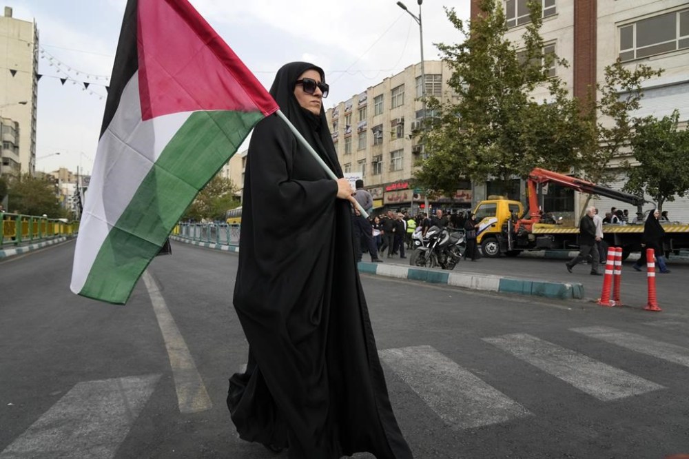 An Iranian woman, carrying a Palestinian flag, walks to attend the funeral ceremony of Hamas leader Ismail Haniyeh and his bodyguard, at Enqelab-e-Eslami (Islamic Revolution) Sq. in Tehran, Iran, Thursday, Aug. 1, 2024. (AP Photo/Vahid Salemi)