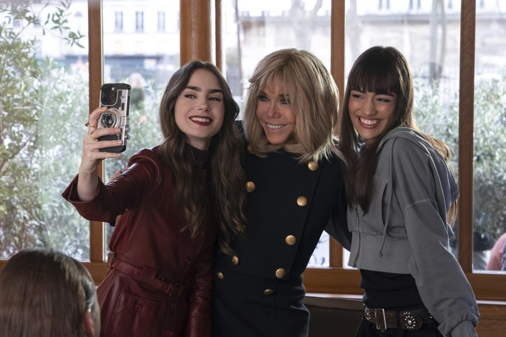 In this his handout photo taken by Stephanie Branchu for Netflix on April 2, 2024, in Paris, Lily Collins, left, French President Emmanuel Macron's wife Brigitte Macron, center, and Thalia Besson pose for a selfie during the shooting of episode 407 of Netflix series