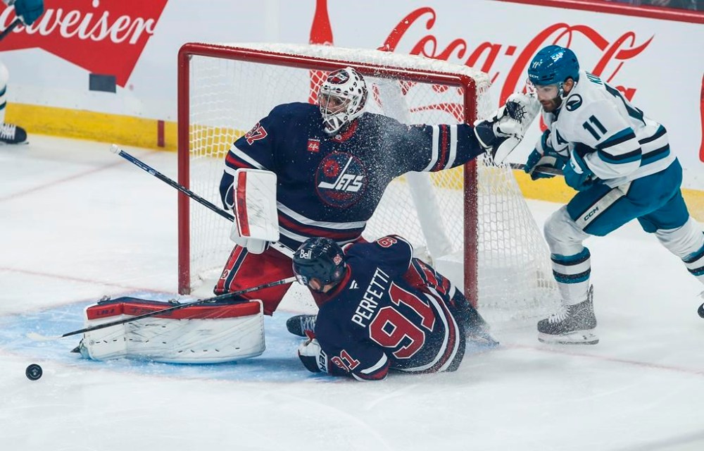 Winnipeg Jets goaltender Connor Hellebuyck (37) saves the shot from San Jose Sharks' Luke Kunin (11) as Cole Perfetti (91) defends during first period NHL action in Winnipeg on Friday, October 18, 2024. THE CANADIAN PRESS/John Woods