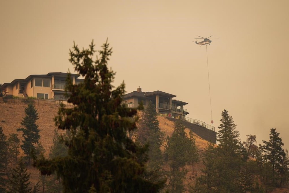 A helicopter with a water bucket flies past homes in the Wilden neighbourhood near Knox Mountain after RCMP officers enforced a new wildfire evacuation order, in Kelowna, B.C., Friday, Aug. 18, 2023. THE CANADIAN PRESS/Darryl Dyck