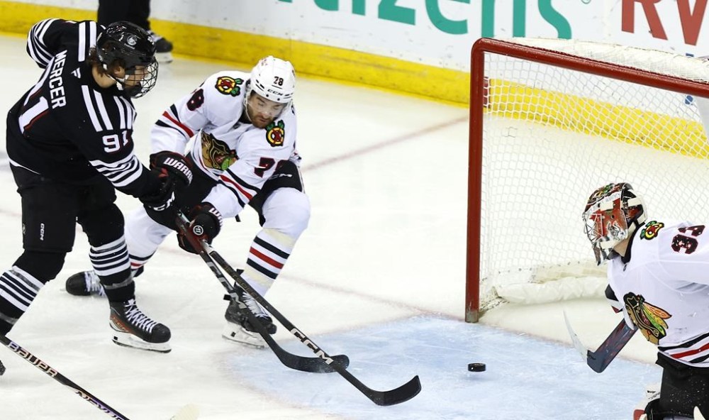 New Jersey Devils center Dawson Mercer (91) scores a goal past Chicago Blackhawks defenseman TJ Brodie (78) and goaltender Drew Commesso (33) during the third period of an NHL hockey game, Saturday, Dec. 14, 2024, in Newark, N.J. The New Jersey Devils won 4-1. (AP Photo/Noah K. Murray)