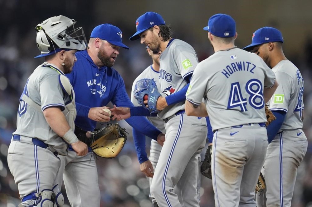 Toronto Blue Jays starting pitcher Kevin Gausman, center, hands the game ball to manager John Schneider for a pitching change during the sixth inning of a baseball game against the Minnesota Twins, in Minneapolis, Friday, Aug. 30, 2024. THE CANADIAN PRESS/AP-Abbie Parr