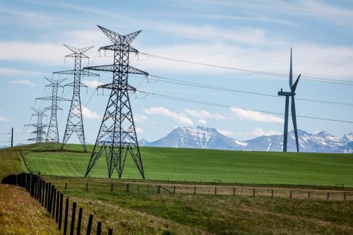 Power transmission lines and wind turbines as seen with the Rocky Mountains in the background near Pincher Creek, Alta., Thursday, June 6, 2024. THE CANADIAN PRESS/Jeff McIntosh