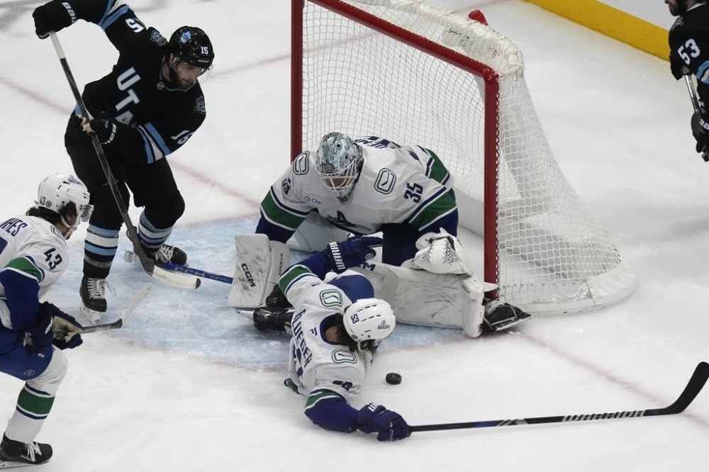 Utah Hockey Club center Alexander Kerfoot (15) looks on as Vancouver Canucks' goaltender Thatcher Demko (35) and Teddy Blueger (53) make a save against Utah Hockey Club during the first period of an NHL hockey game Wednesday, Dec. 18, 2024, in Salt Lake City. (AP Photo/Rick Bowmer)
