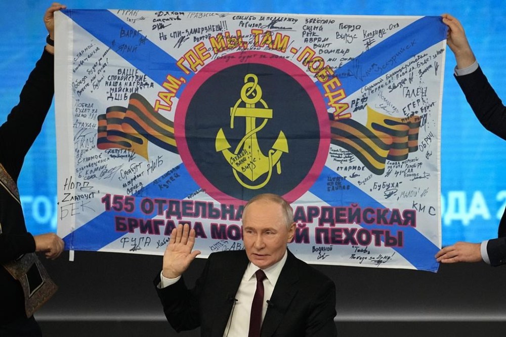 Russian President Vladimir Putin speaks during his annual news conference and call-in show at Gostinny Dvor in Moscow, Russia, Thursday, Dec. 19, 2024, as men hold a replica of the banner of the 155th Marine Brigade of the Pacific Fleet, participating in a special military operation in Ukraine in the background. (AP Photo/Alexander Zemlianichenko)